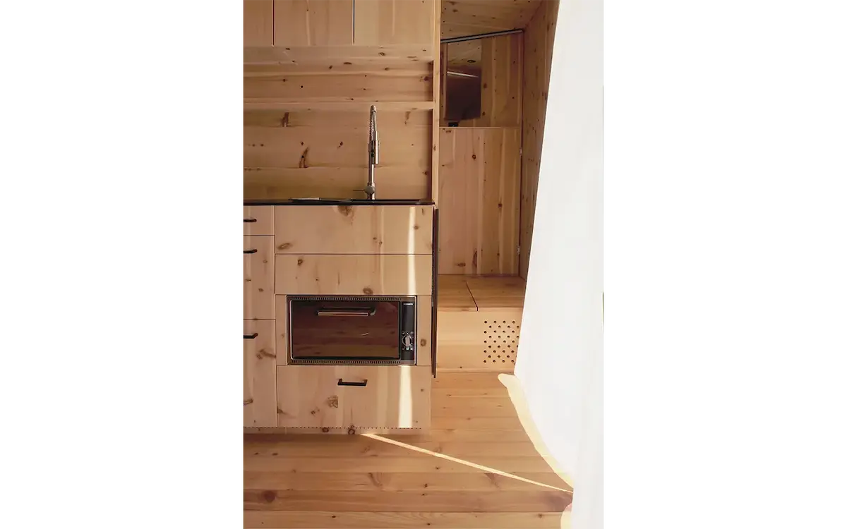 Detailansicht der Küche im Ikarus-Wohnwagen mit eingebautem Backofen, Holzschubladen und Spülbecken in hellem Fichtenholz